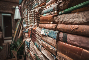 A unique display of old books stacked on a slanted wall in Venice, Italy. The vintage arrangement...