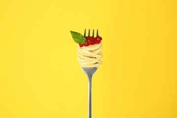 Fork with tasty pasta, tomato sauce and basil on yellow background