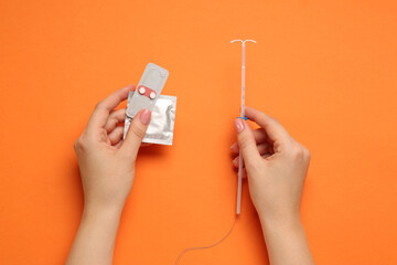 Woman with condom, contraceptive pills and intrauterine device on orange background, top view....