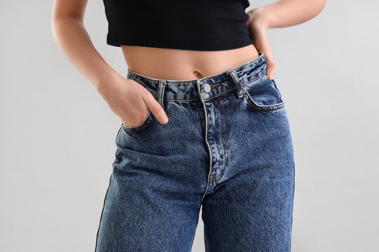 Young woman in dark blue jeans on light background, closeup