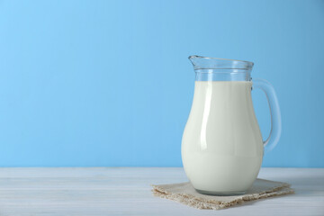 Jug of fresh milk on white wooden table against light blue background, space for text