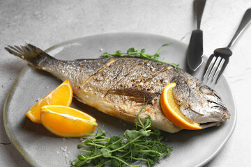 Seafood. Delicious baked fish served with orange and microgreens on light textured table, closeup