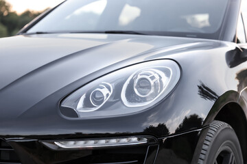 Fototapeta premium Modern black car parked outdoors, closeup view of headlight