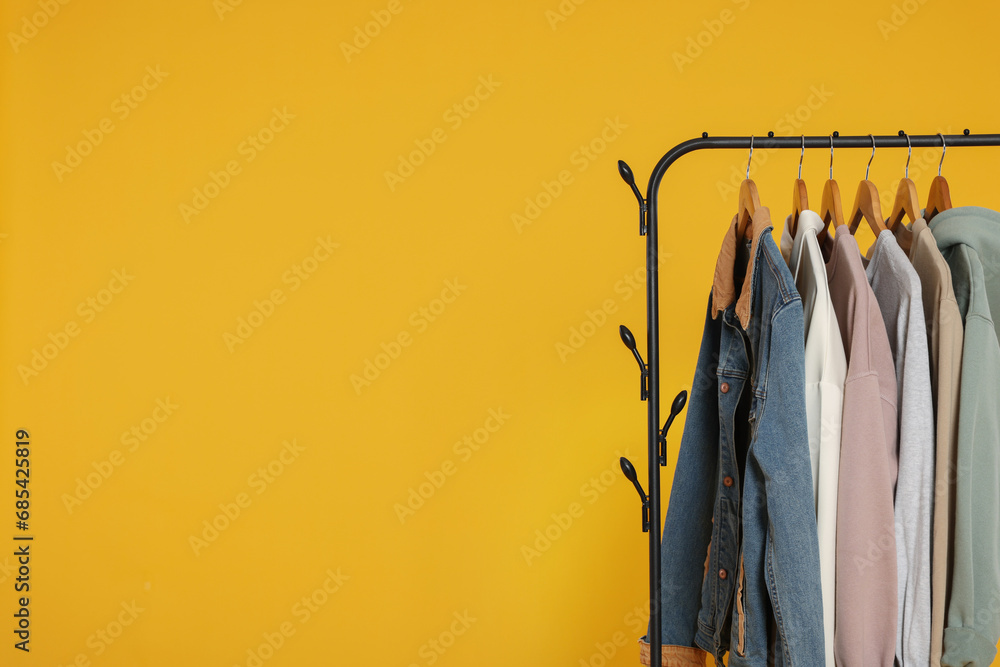 Wall mural Rack with stylish clothes on wooden hangers against orange background, space for text - Wall murals
