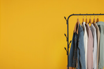 Rack with stylish clothes on wooden hangers against orange background, space for text
