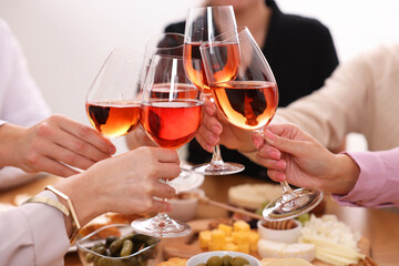 People clinking glasses with rose wine above table indoors, closeup