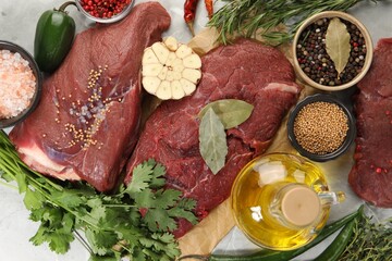 Pieces of raw beef meat, herbs and spices on light grey table, flat lay