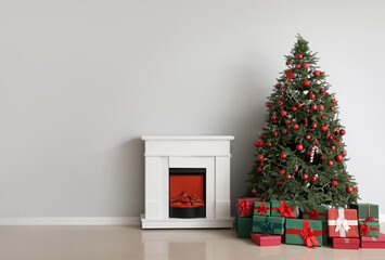 Christmas tree with ornaments, gift boxes and fireplace near white wall