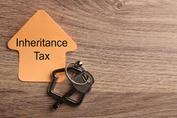 Inheritance Tax. Sticky note and key with key chain in shape of house on wooden table, flat lay....