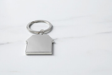 Metal keychain in shape of house on light marble table. Space for text