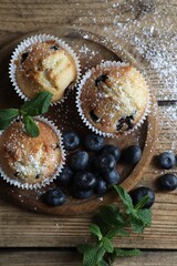 Obraz na płótnie Canvas Delicious muffins powdered with sugar, blueberries and mint on wooden table, flat lay