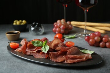 Delicious bresaola, tomato and basil leaves on grey textured table