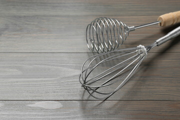 Two metal whisks on wooden table, closeup. Space for text