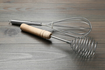 Two metal whisks on wooden table, closeup