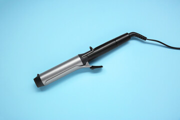 Hair styling appliance. One curling iron on light blue background, top view