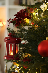Christmas lantern with burning candle on fir tree against blurred background, closeup