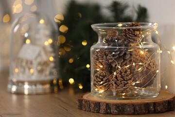 Christmas decoration. Cones and festive lights in jar on wooden table, closeup. Space for text