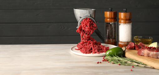 Manual meat grinder with beef mince and other products on light wooden table. Banner design with...