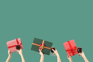 Female hands with glasses of warm mulled wine and gift boxes on green background