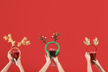 Female hands with glasses of warm mulled wine and Christmas reindeer horns on red background