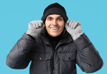 Young man in stylish puffer jacket and gloves on blue background