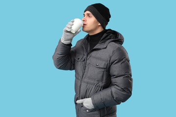 Young man in stylish puffer jacket with paper cup of coffee on blue background