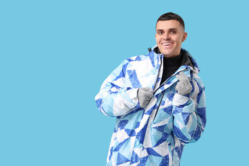 Young man in stylish puffer jacket and gloves on blue background