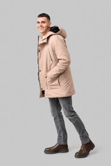 Smiling young man in stylish beige winter parka and gray jeans, casual fashion and cold weather apparel © Pixel-Shot