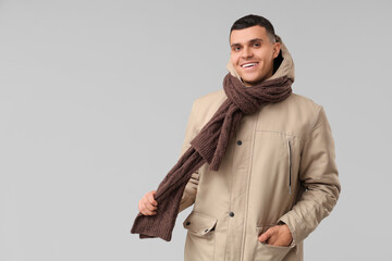 Young man in stylish puffer jacket and scarf on grey background