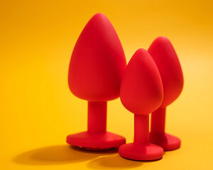 Three size silicone red butt plugs on an orange background.