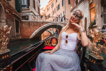 A serene gondola ride in Venice, Italy. A woman enjoys the picturesque scenery of traditional Venetian architecture and charming buildings lining the canal on a warm, sunny day.