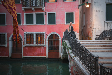 A romantic couple stands on a picturesque bridge in Venice, Italy, surrounded by charming historic...