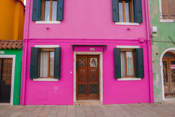 Vibrant pink house in Burano, Italy, with no landmarks or signage. Surrounding houses and material are unknown. No water, bridges, or vegetation visible.