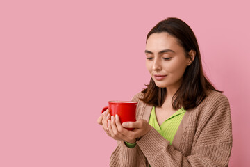 Beautiful young woman with cup of hot mulled wine on pink background