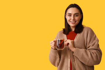 Happy young woman with glass cup of hot mulled wine on yellow background
