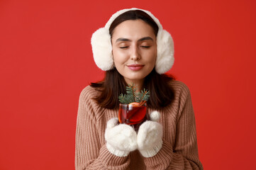 Beautiful young woman in warm mittens with glass of hot mulled wine on red background