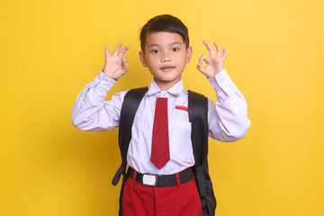 Asian school boy in uniform showing ok sign over yellow background