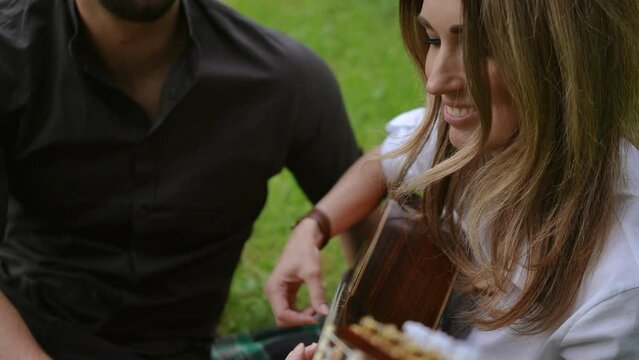 Close-up. Happy woman playing guitar for her lover while sitting on the grass in a city park