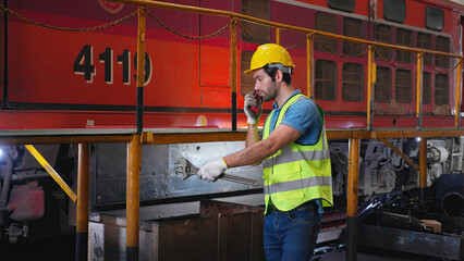 Young caucasian engineer man maintenance and repair train diesel engine while using talkie with command to worker in station, engineer inspect system transport, transportation and industry.