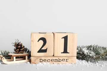 Cube calendar with date of winter solstice, wooden sledge, fir cone, branches and snow on light...