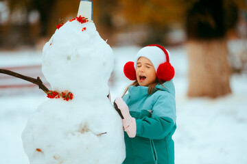 Cheerful Little Girl Enjoying Winter Building a Snowman. Happy child feeling excited about having...