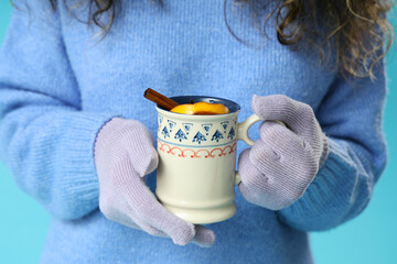 Young African-American woman in gloves with cup of hot mulled wine on blue background