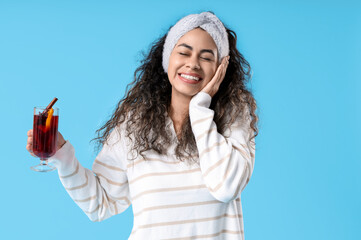 Happy young African-American woman with glass cup of hot mulled wine on blue background