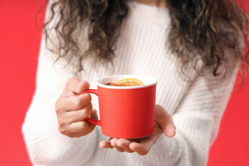 Young African-American woman with cup of hot mulled wine on red background