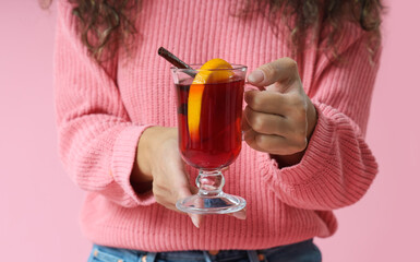 Young African-American woman with glass cup of hot mulled wine on pink background