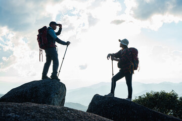 Silhouette of Asian Male and female standing with trekking poles on cliff edge on top of rock...