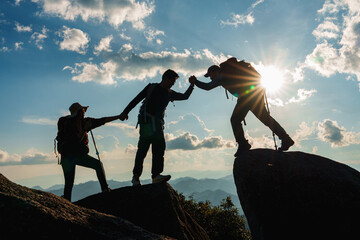 Silhouette of Asian teamwork  hikers climbing up mountain cliff and one of them giving helping hand on top of rock mountain with beautiful sunset background, People helping,  - obrazy, fototapety, plakaty