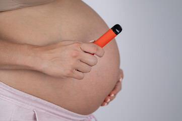 A pregnant woman smokes a vape. A girl holds an electronic cigarette against the background of her...