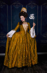 18th century woman wearing a gold silk dress and holding a small mask