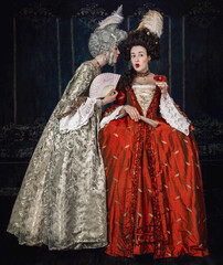 Two 18th century women standing close together gossiping 